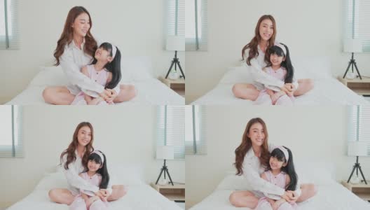 母亲和小女儿坐在家里卧室的床上。有魅力的漂亮的妈妈花时间与小女孩在清晨看相机。家庭关系概念。高清在线视频素材下载