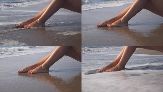 海浪冲刷着女性晒黑的脚。性感女孩的腿躺在海边的金色沙滩上，放松在暑假旅行。旅行的概念。慢动作关闭低角度视图侧视图高清在线视频素材下载