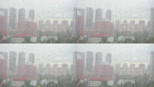 潮湿的窗玻璃，雨点落在模糊的城市背景下的窗玻璃表面高清在线视频素材下载