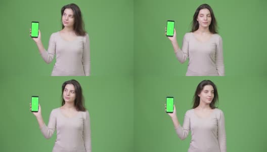 年轻美丽的女人思考，而显示手机对绿色的背景高清在线视频素材下载