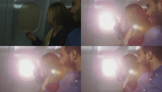 在一架商用飞机上，美丽的金发乘客打开窗帘，叫醒了正在睡觉的西班牙男性邻居。新飞机有漂亮的内部设计。高清在线视频素材下载