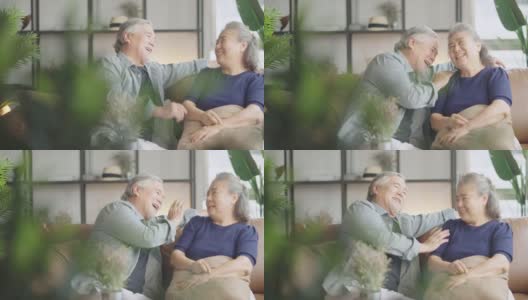 亚洲老老人退休夫妇享受在沙发上谈笑风生，在家里开心地笑着，亚洲老成年人居家隔离期的概念高清在线视频素材下载