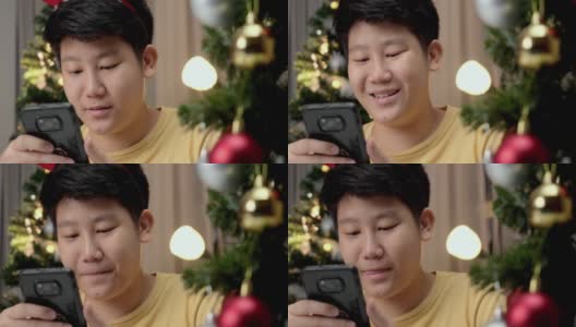 亚洲男孩在圣诞节的灯光背景下，晚上在家玩手机游戏。高清在线视频素材下载
