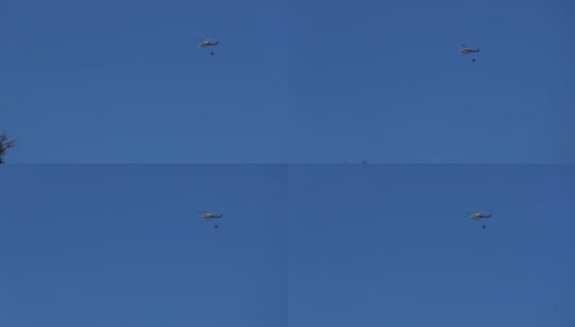 一架载着水箱的直升机在正午的蓝天上飞行高清在线视频素材下载