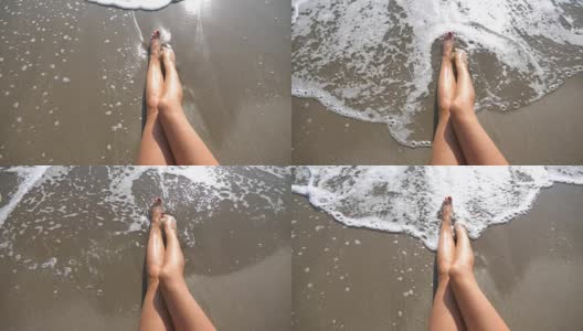 海浪冲刷着晒黑的女性脚。在一个阳光明媚的日子里，一个美丽的女孩躺在沙滩上。暑假期间，一个陌生的年轻女子在海边放松。俯视图慢动作特写高清在线视频素材下载