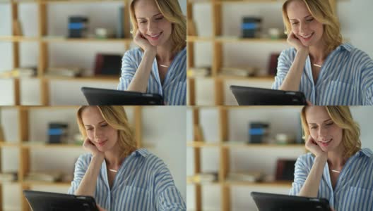 笑容满面的女士看着平板电脑，同时在家里学习高清在线视频素材下载
