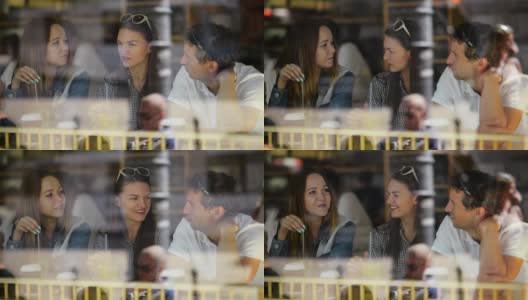 一个黑发女人和两个朋友坐在咖啡馆，喝着饮料聊天。透过餐厅的窗户看到三个朋友高清在线视频素材下载