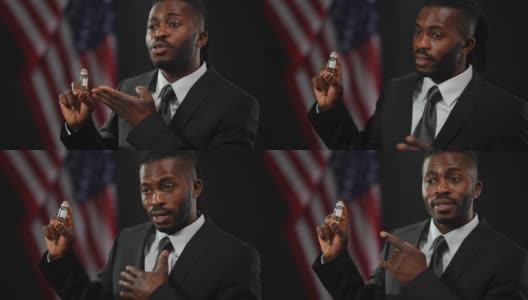 一名非洲裔美国男性政客正在为新冠疫苗注射做广告，背景是美国国旗。一个严肃自信的男人的肖像，穿着正式的黑色西装，谈论疫苗接种的需要。高清在线视频素材下载
