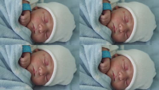 新生儿脸部肖像痤疮过敏刺激早期睡眠在蓝色背景。在帽子上的生命开始分钟的孩子。婴儿，分娩，出生的最初时刻，开始的概念高清在线视频素材下载