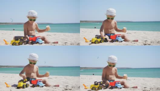 一个阳光明媚的夏日，一个男孩在沙滩上玩沙子和玩具、汽车。一个孩子坐在以蔚蓝大海为背景的沙滩上吃冰淇淋高清在线视频素材下载