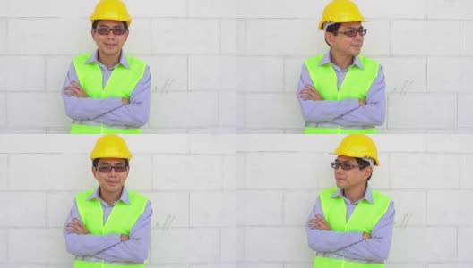 亚洲男性工人微笑着看着相机，双臂交叉，自信的劳动快乐在建筑工地，职业就业高清在线视频素材下载