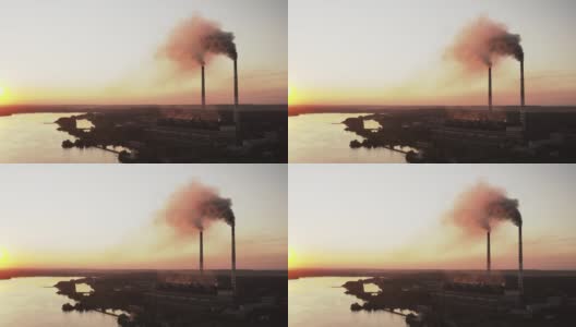 黄昏时河边的有害工厂。夕阳西下时，烟囱向空中喷出黑烟的工业区。环境污染。鸟瞰图。高清在线视频素材下载