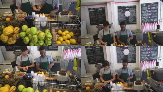 果汁吧的员工们像一个团队一样工作，一个传递水果，另一个切水果，玩得很开心高清在线视频素材下载