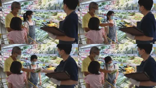 一位亚洲华人中年女性零售助理，建议并帮助一个家庭从超市的冷藏区选择蔬菜高清在线视频素材下载