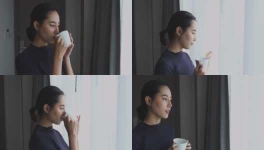 亚洲女人喝咖啡，看着窗外的房子。高清在线视频素材下载