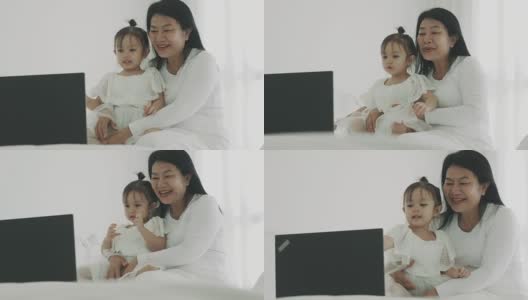 一位泰国母亲带着她的宝贝女儿在她的房间里用笔记本电脑看卡通片高清在线视频素材下载