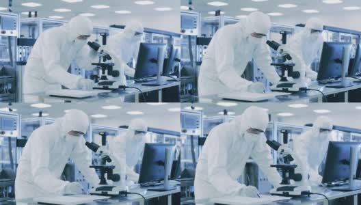 在实验室，科学家穿着防护服做研究，使用显微镜和输入数据到个人电脑。现代制造半导体和制药项目。高清在线视频素材下载