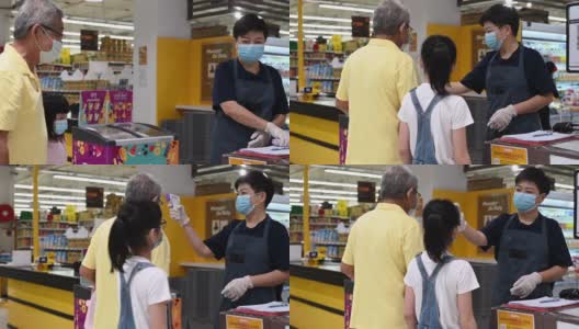 一名亚洲华人中年妇女店主在进入超市前测量老年男子前额测量体温作为新冠肺炎安全预防的标准操作程序高清在线视频素材下载