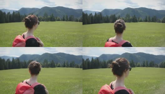 年轻女孩背着背包，穿过绿色的草地，背景是群山高清在线视频素材下载