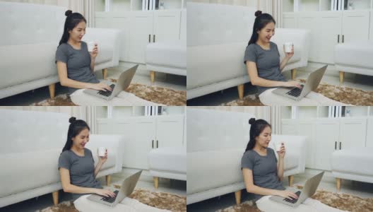 一位亚洲妇女坐在客厅里，手里拿着一个咖啡杯，膝上放着一台笔记本电脑。高清在线视频素材下载