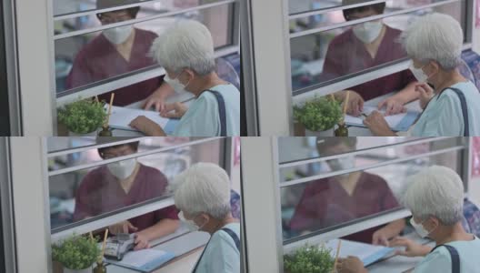 亚洲华人老年女性，戴着防护口罩，用信用卡支付医疗费用，在NFT诊所女护士持有的信用卡读卡器上点击高清在线视频素材下载