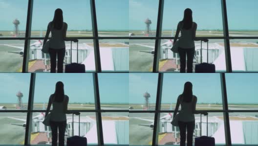 一个女人带着行李箱站在机场候机楼看窗外的剪影高清在线视频素材下载