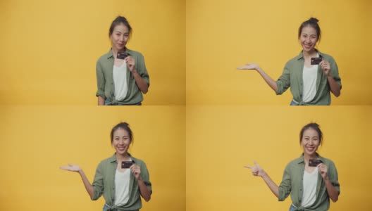 美丽迷人的亚洲青年孤立的女士看空的空间手握信用卡网上购买网上购物成功支付在黄色背景。高清在线视频素材下载