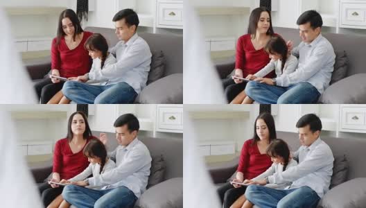 母亲和父亲看着男孩在触控板上玩游戏。幸福和友好的家庭，家人一起在家里度过时光。幸福的家庭。有趣的脸高清在线视频素材下载