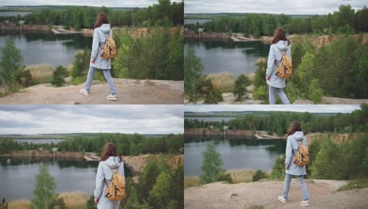 一名年轻的红发女子走到悬崖边，观看令人兴奋的湖泊、树林和建筑物的慢动作肖像。美丽的自然和旅游理念。高清在线视频素材下载