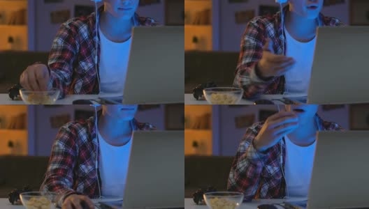 男游戏玩家戴着耳机和网友聊天，吃着玉米片高清在线视频素材下载