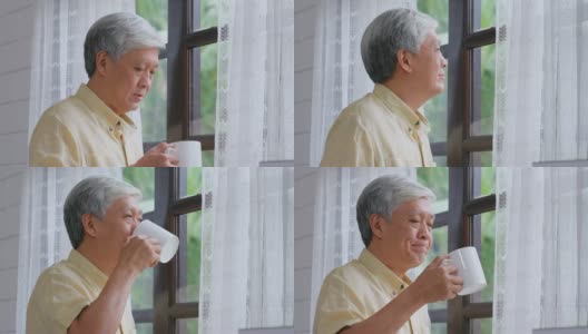 年长的亚洲男人站在窗边喝咖啡，放松情绪，退休生活高清在线视频素材下载
