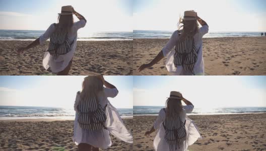 不认识快乐的女孩在比基尼和衬衫与背包在海滩上跑到大海。美丽的女人慢跑和拿着帽子与她的手在阳光灿烂的日子。年轻的女士享受生活，享受日出。近景后视图慢动作高清在线视频素材下载