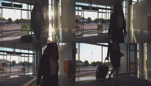 商务女士带着行李去机场。穿着高跟鞋的年轻女子穿过玻璃门进入航站楼，用轮子推着行李箱。旅行或度假旅游概念。慢镜头高清在线视频素材下载