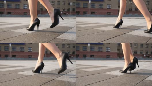 在阳光明媚的日子里，穿着黑色高跟鞋的苗条女性的腿走在城市广场上。年轻女商人的脚穿着高跟鞋走在城市的街道上。低角度视角慢动作特写高清在线视频素材下载