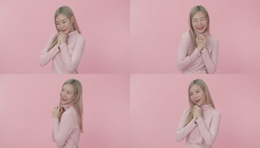 照片中的年轻害羞和美丽的亚洲女子在粉红色的长袖t恤牵手，看着和尴尬的微笑在粉红色的背景相机。情感和身体语言的概念。高清在线视频素材下载