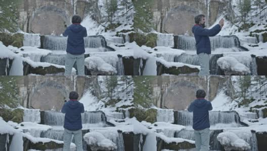 独自一人在自然。一名男性游客在冬季拍摄美丽的冰冻瀑布。旅行和摄影。高清在线视频素材下载