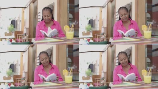 高级非洲妇女在户外早午餐时间在酒吧餐厅阅读一本书的乐趣高清在线视频素材下载