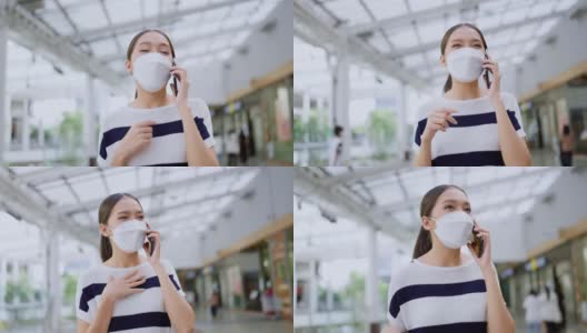 快乐微笑的亚洲女性戴着口罩交流交谈智能手机，亚洲女性走在户外广场百货商店享受放松聊天与她的朋友通过智能手机高清在线视频素材下载
