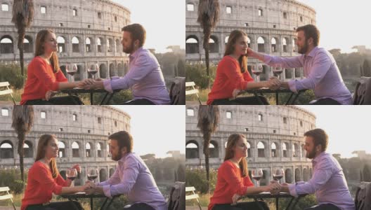 日落时分，浪漫优雅的情侣坐在罗马斗牛场前的餐厅桌前，手里拿着一杯红酒，手拉手交谈高清在线视频素材下载
