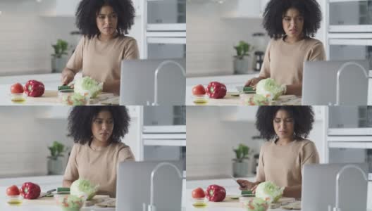 一段4k视频记录了一名年轻女子在家里用笔记本电脑准备一顿健康大餐高清在线视频素材下载