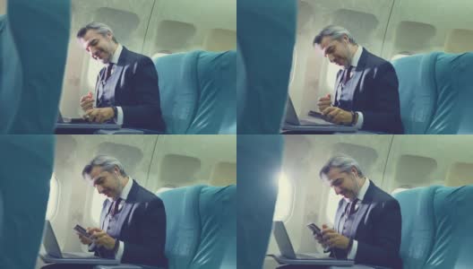 一位亚洲高管商人坐在商务头等舱，在飞机上用笔记本电脑工作。这名男子喜欢用手机听音乐，独自坐在飞机上感觉放松、快乐和快乐。高清在线视频素材下载