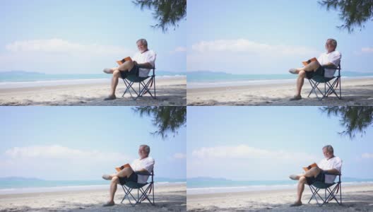 一位亚洲老人坐在海边的户外椅上，享受着看书的乐趣。高清在线视频素材下载