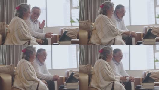 老亚洲老夫妇退休年龄坐在沙发沙发上视频给他们的家人打电话用平板设备社交连接家隔离呆家状态秩序概念，幸福老笑快乐高清在线视频素材下载