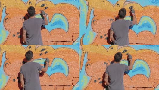 英俊的天才小男孩用喷雾剂在城市的街道墙上涂鸦。电影色调的慢动作镜头。创造性的艺术。后视图，总体规划高清在线视频素材下载