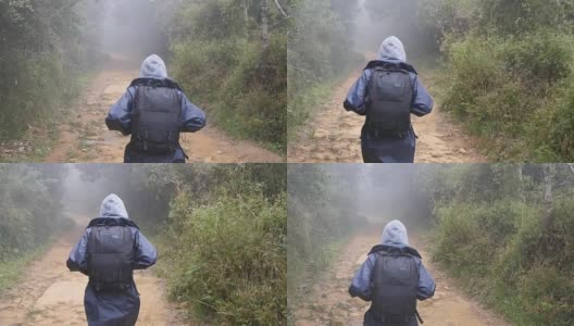 徒步女子与背包跑在热带潮湿的森林。年轻的女孩在旅行中穿着雨衣在木头小径上慢跑。跟随女游客踩在丛林小径。慢镜头后视图高清在线视频素材下载