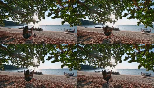 年轻女子在海滩上的木秋千上休息在树荫下高清在线视频素材下载