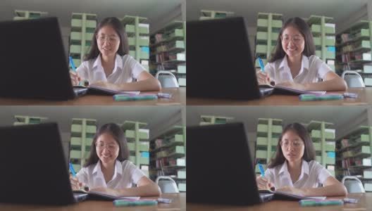 亚洲大学生女孩读书和工作用笔记本电脑和智能手机做她的家庭作业在公共图书馆高清在线视频素材下载