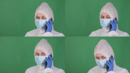 年轻的女医务人员在一个绿色的背景下讲电话，在一个白色的雾大衣防护面具和橡胶手套高清在线视频素材下载