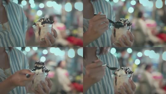 一个亚洲女人在夜市吃着美味的冰淇淋甜点。泰国著名的美食街甜品。泰国的街头小吃。高清在线视频素材下载