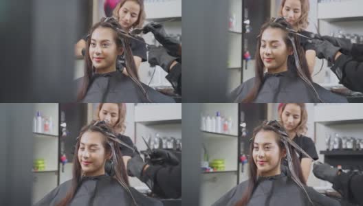 年轻的亚洲美丽的女孩在沙龙改变发型和颜色。美发师在美容院给一位女士染发。女人笑着看着镜子。美发美容沙龙概念。高清在线视频素材下载